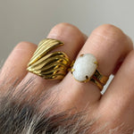 Tendance stacking : accumulation d'une bague sculpturale dorée et d'une bague à pierre blanche portées ensemble au même doigt.