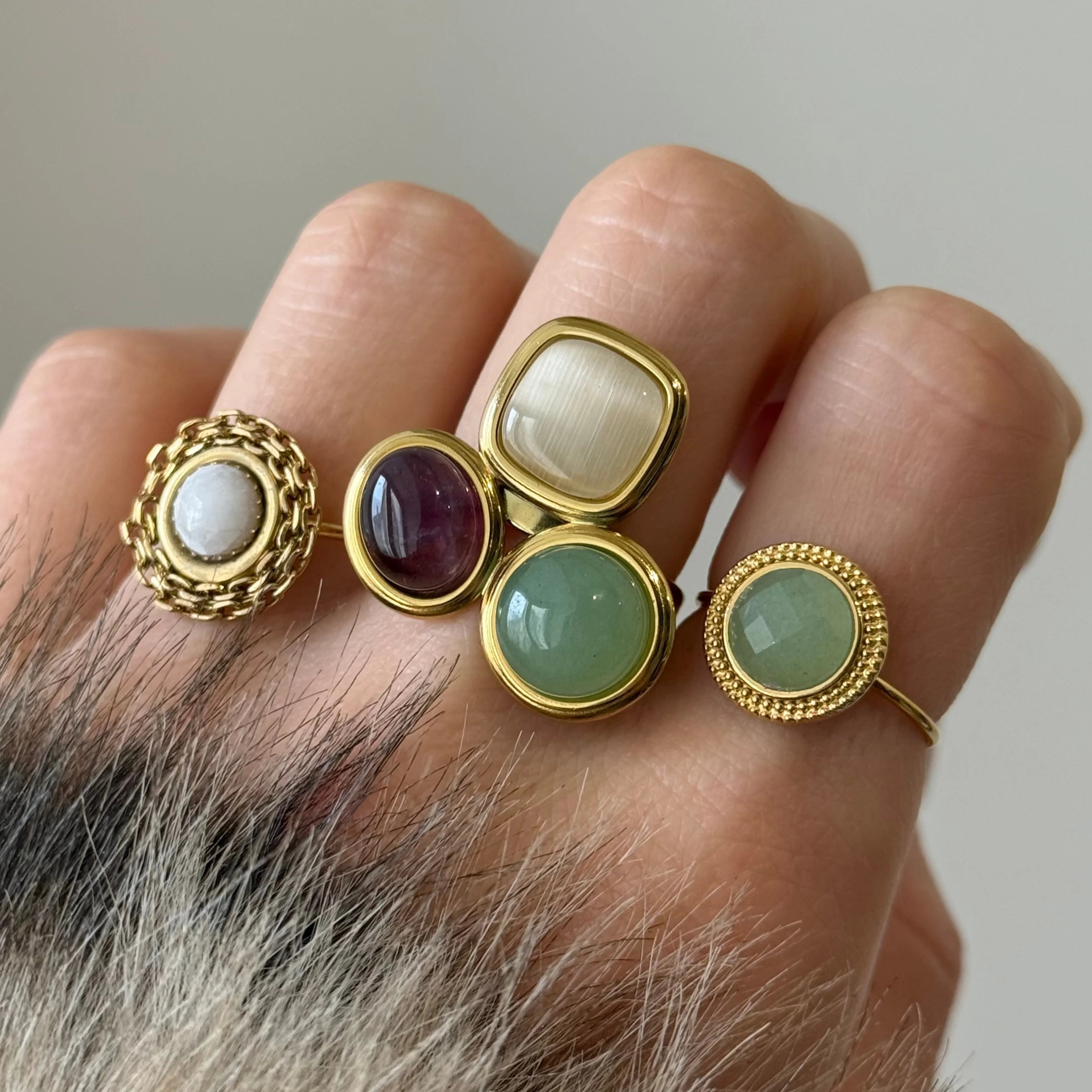 Tendance stacking : zoom sur trois bagues dorées différentes (pierre blanche, verte et trio multicolore) portées ensemble sur la même main.