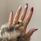 Assortiment complet de bagues dorées serties de pierres naturelles colorées, portées sur une main avec une manucure nail art bordeaux et doré.