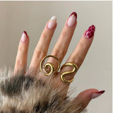 Inspiration look bijoux : association de bagues dorées artistiques aux formes courbes et graphiques.