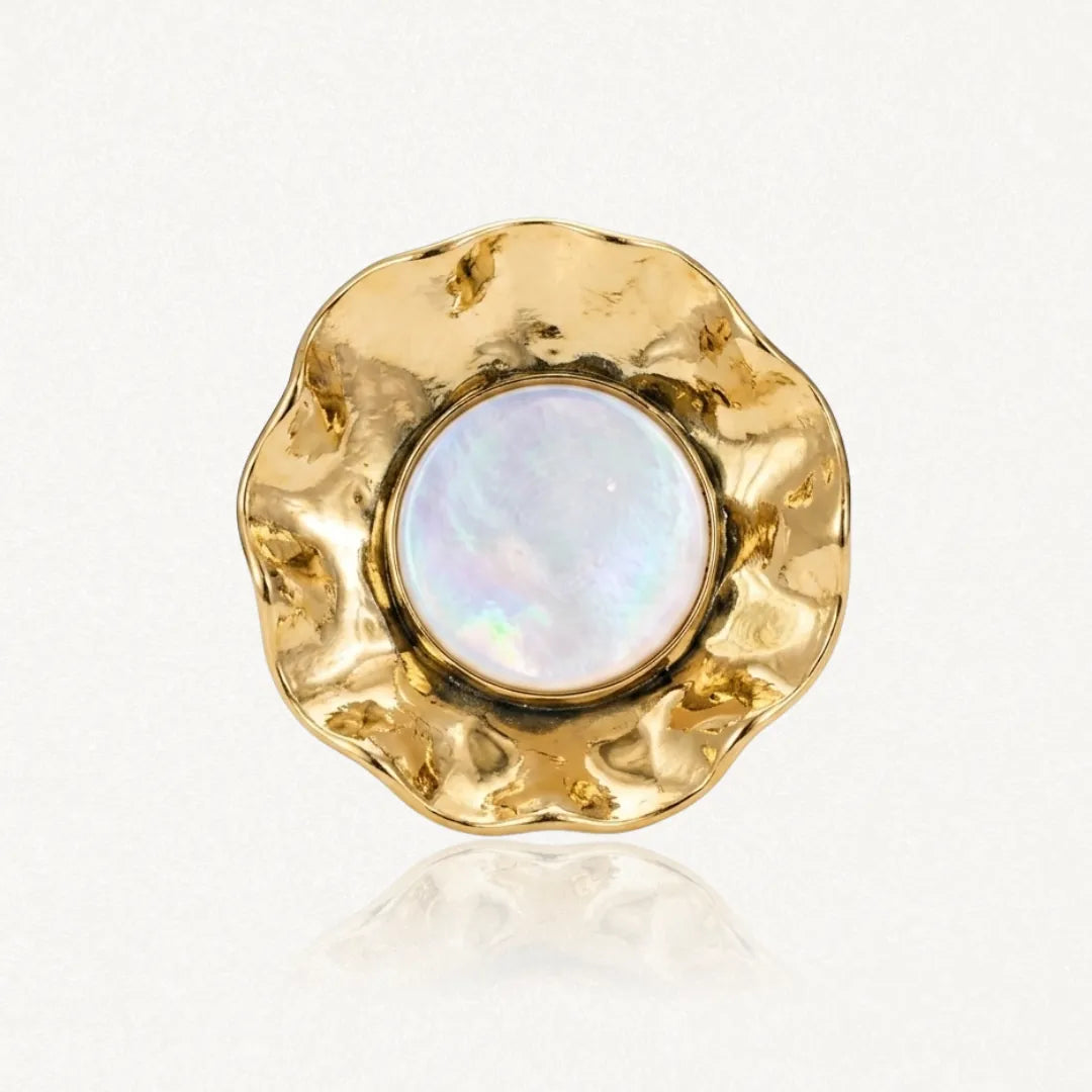 Bague avec un cabochon rond de résine irisée blanche, entouré d'acier inoxydable doré martelé aux bords ondulés.