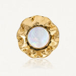 Bague avec un cabochon rond de résine irisée blanche, entouré d'acier inoxydable doré martelé aux bords ondulés.