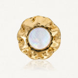 Bague avec un cabochon rond de résine irisée blanche, entouré d'acier inoxydable doré martelé aux bords ondulés.