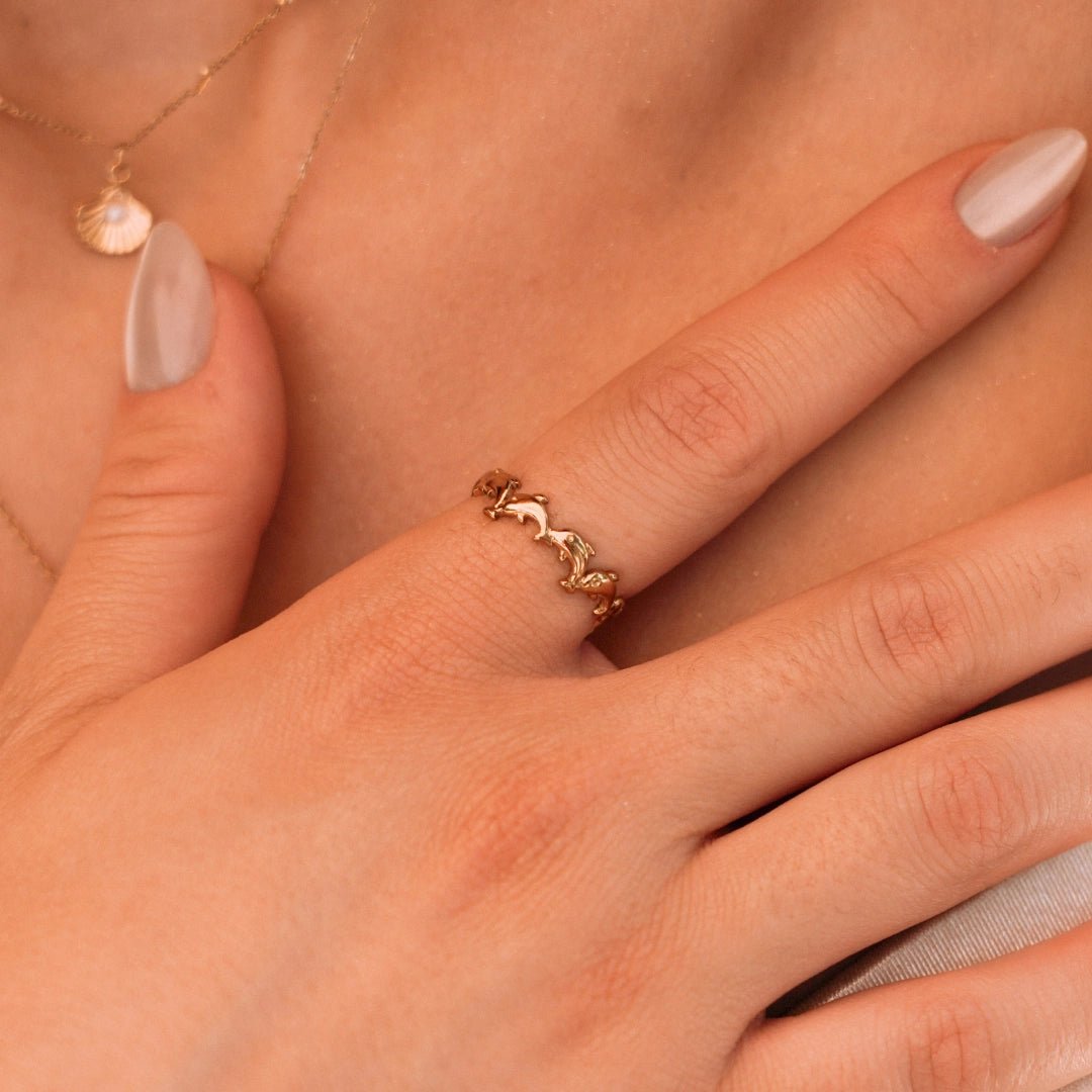 Bague en acier inoxydable couleur or avec dauphins entrelacés, portée sur le doigt d'une femme.