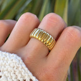 Bague acier inoxydable doré, large design nervuré style croissant, portée sur doigt avec pull blanc.