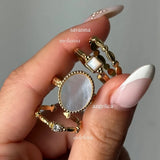 Bague ANGELICA solitaire en acier inoxydable doré, ornée d'un zirconium central rond à la surface irisée, tenue par une main.