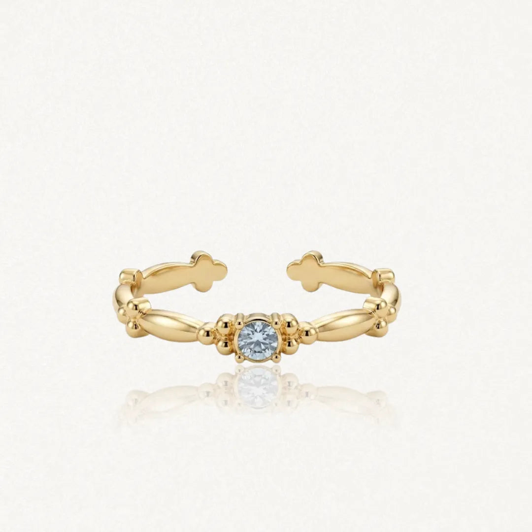 Bague ajustable en acier inoxydable doré avec zirconium solitaire bleu clair, ornée de motifs de petites billes et trèfles.