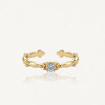 Bague ajustable en acier inoxydable doré avec zirconium solitaire bleu clair, ornée de motifs de petites billes et trèfles.