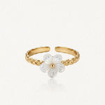 Bague ajustable en acier inoxydable doré à l'anneau gravé, ornée d'une fleur de nacre blanche au cœur doré.