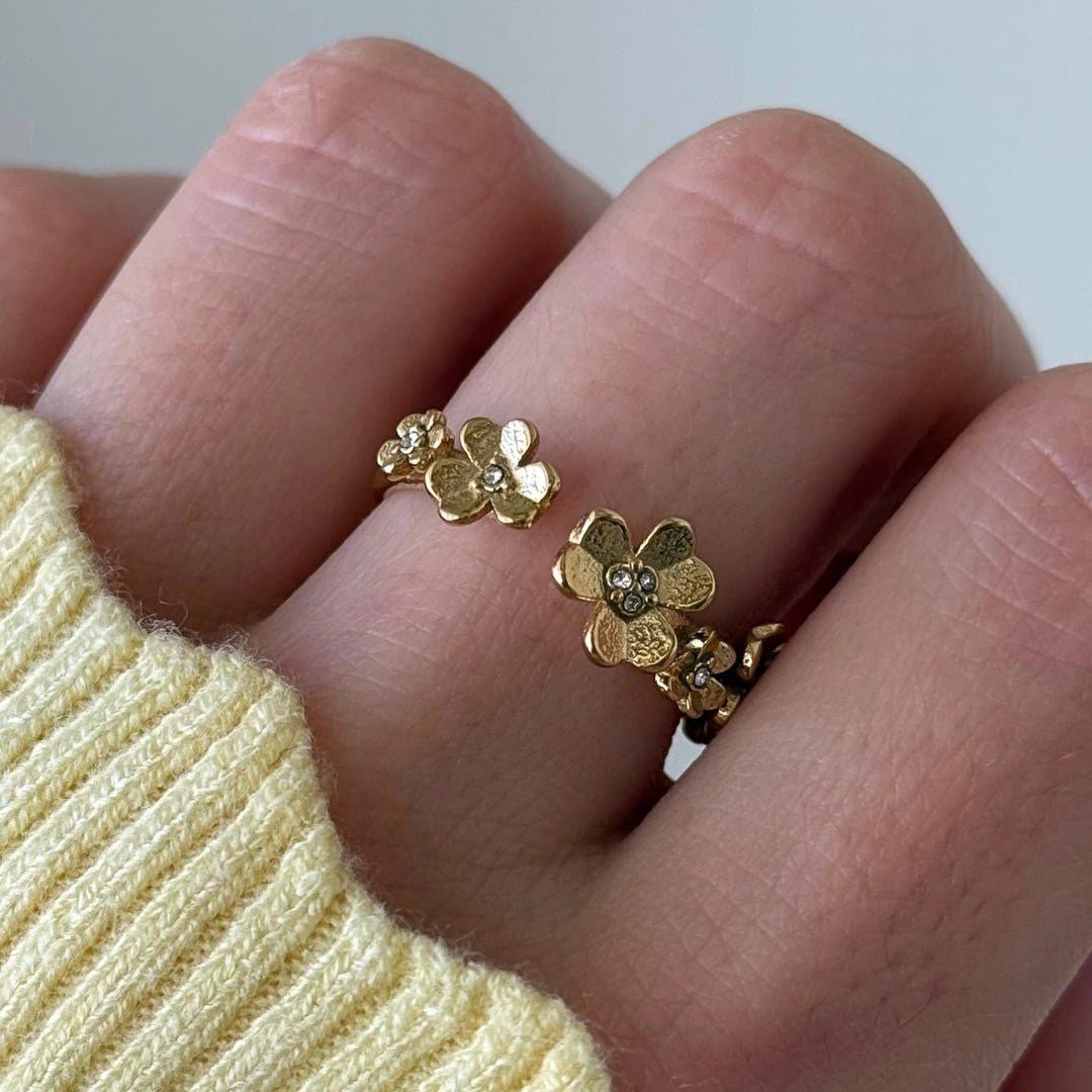Bague ouverte en acier inoxydable doré, composée de fleurs détaillées avec strass centraux, portée sur un doigt.