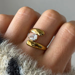 Bague ouverte en acier inoxydable doré, avec un Zirconium taille poire serti entre deux sections arrondies. Main avec manche
