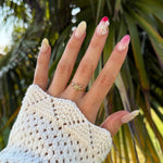 Bague en acier inoxydable dorée avec motif étoile de mer, portée sur une main avec des ongles colorés et une manche blanche.