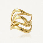 Bague en acier inoxydable doré, design ondulé à trois bandes lisses et brillantes sur fond blanc.