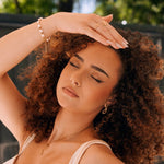 Bague en acier inoxydable doré, motif végétal ajouré, sur la main d'une femme aux cheveux bouclés.
