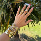Main de femme avec bagues et bracelets en acier inoxydable doré; une bague fleur de cerisier et une avec cabochon blanc.