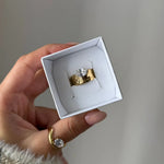 Main tenant une boîte blanche avec bague chevalière en acier inoxydable doré organique martelée et zirconium. Une bague