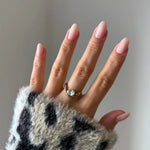 Main avec pull imprimé léopard, portant une bague chevron ouverte en acier inoxydable doré et zirconium rond.