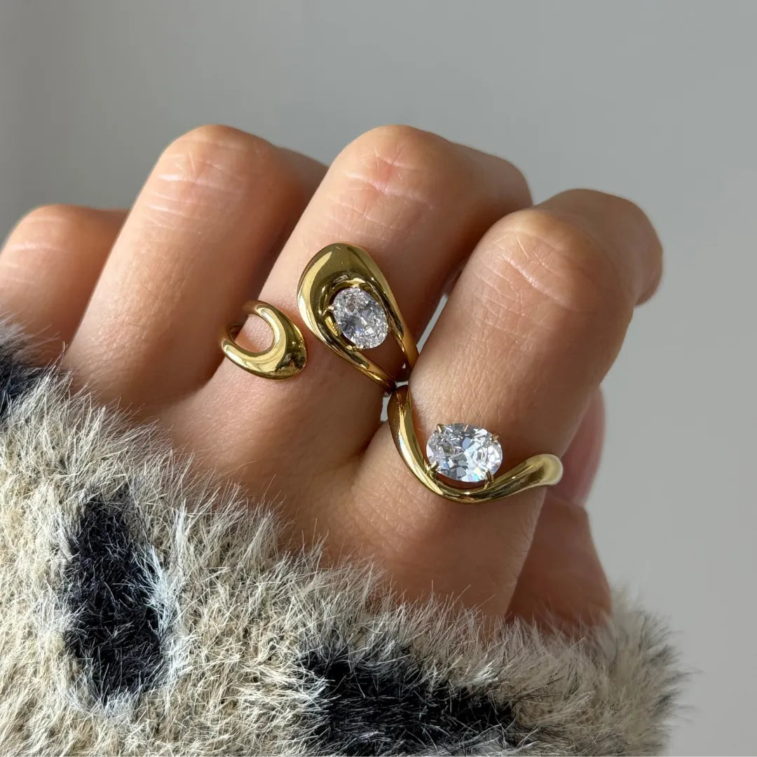 Bague ouverte en acier inoxydable doré avec deux Zirconium ovales étincelants, portée au doigt sur un pull doux.