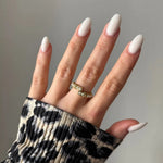 Bague dorée ouverte ornée de petites perles blanches sur annulaire, main aux ongles ovales blancs, manche imprimé léopard.