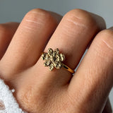 Bague en acier inoxydable doré avec une fleur texturée de 1,20 cm de haut, portée sur un doigt.