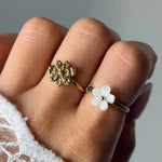 Deux bagues en acier inoxydable doré: une fleur texturée, et une fleur en nacre blanche sur bande texturée.