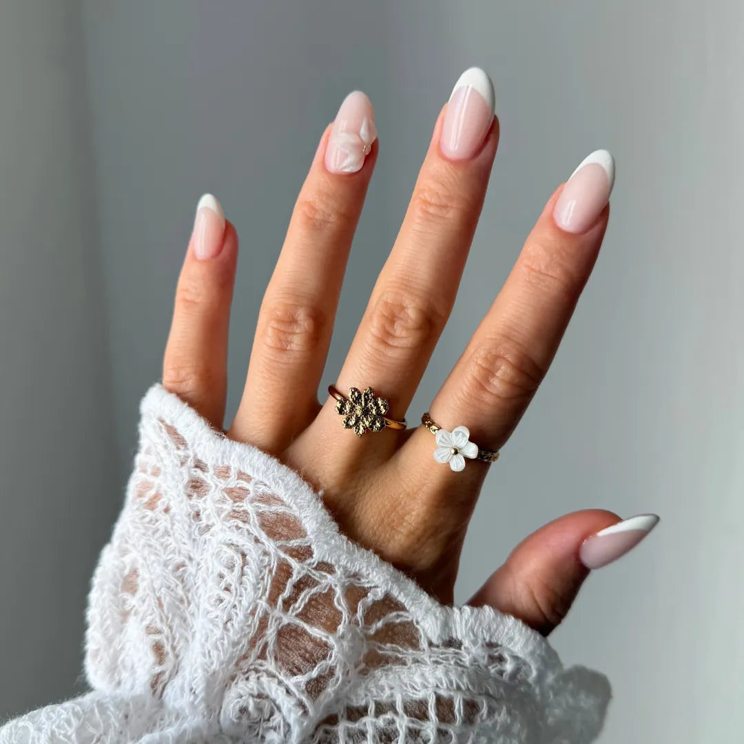 Main en dentelle, ongles manucurés, avec une bague fleur texturée en acier inoxydable doré sur l'index et une bague fleur