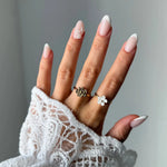 Main en dentelle, ongles manucurés, avec une bague fleur texturée en acier inoxydable doré sur l'index et une bague fleur