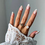 Main en dentelle, ongles manucurés, avec une bague fleur texturée en acier inoxydable doré sur l'index et une bague fleur
