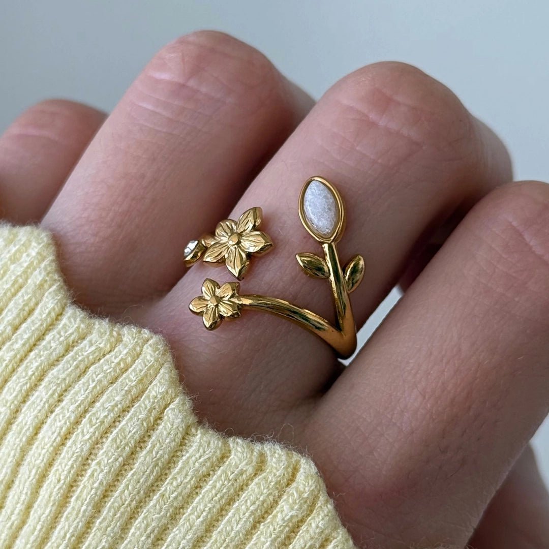 Bague réglable en acier inoxydable doré, motif floral: 2 petites fleurs (une avec strass), tige et pierre blanche ovale.