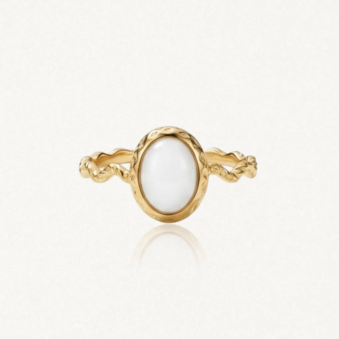 Bague dorée avec un anneau torsadé et une pierre ovale blanche opaque, sertie d'un rebord doré martelé.