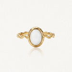 Bague dorée avec un anneau torsadé et une pierre ovale blanche opaque, sertie d'un rebord doré martelé.