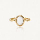 Bague dorée avec un anneau torsadé et une pierre ovale blanche opaque, sertie d'un rebord doré martelé.