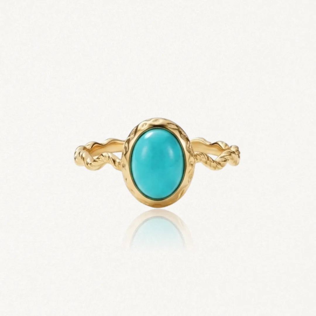 Bague dorée avec un anneau torsadé et une pierre ovale turquoise au centre, sertie dans une monture dorée texturée.