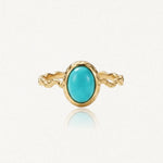 Bague dorée avec un anneau torsadé et une pierre ovale turquoise au centre, sertie dans une monture dorée texturée.
