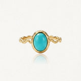 Bague dorée avec un anneau torsadé et une pierre ovale turquoise au centre, sertie dans une monture dorée texturée.