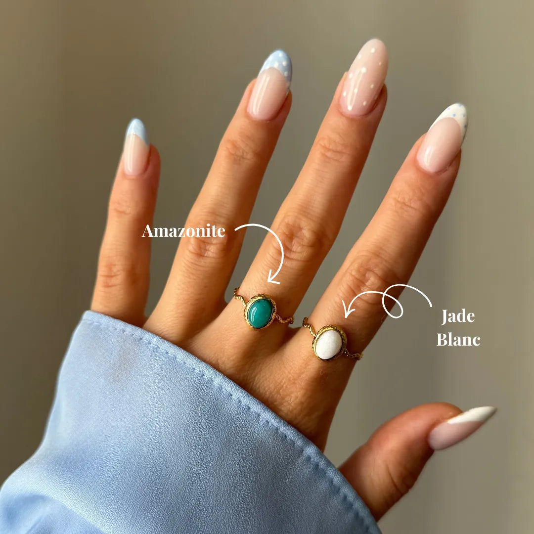 Main aux ongles manucurés portant deux bagues dorées. L'une avec une amazonite ovale turquoise, l'autre avec un jade blanc