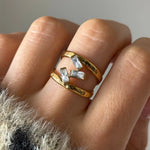 Bague double anneau en acier inoxydable doré, légèrement martelé, ornée de trois zircons baguette. Portée sur un doigt.