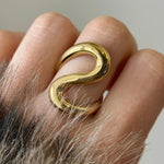 Gros plan sur une bague dorée aux courbes organiques et volumineuses portée à l'index.