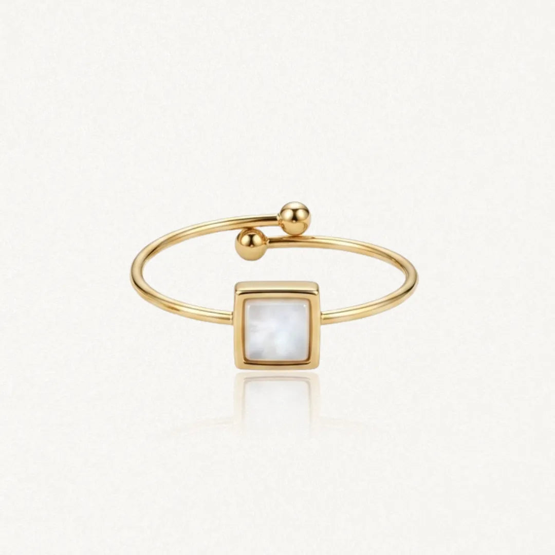 Bague dorée ouverte avec un motif central carré en nacre blanche. Une extrémité est ornée de deux billes dorées, l'autre