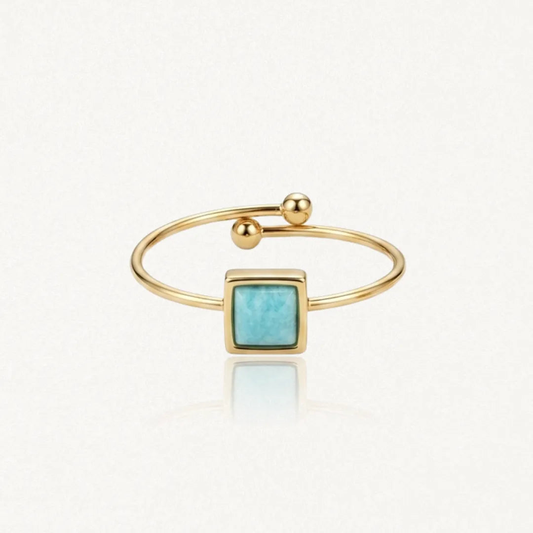 Bague ouverte dorée avec une pierre carrée bleu-vert au centre et des billes aux extrémités.