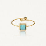Bague ouverte dorée avec une pierre carrée bleu-vert au centre et des billes aux extrémités.