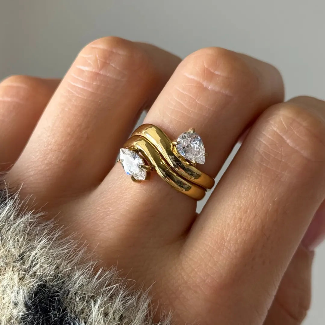 Bague double rang ondulé en acier inoxydable doré, deux zirconiums (poire et marquise) portée au doigt.
