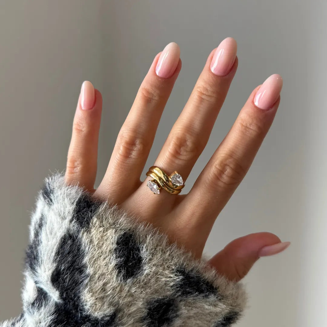 Main féminine portant une bague double rang en acier inoxydable doré ornée de deux zirconiums taille poire. Manchette