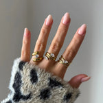 Main, manucure naturelle, portant une bague double rang en acier inoxydable doré, sertie de deux pierres de zirconium poire.