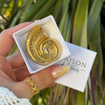 Bague en acier inoxydable doré, motif texturé dentelé, portée au doigt. Une boîte cadeau ouverte avec un pendentif doré en