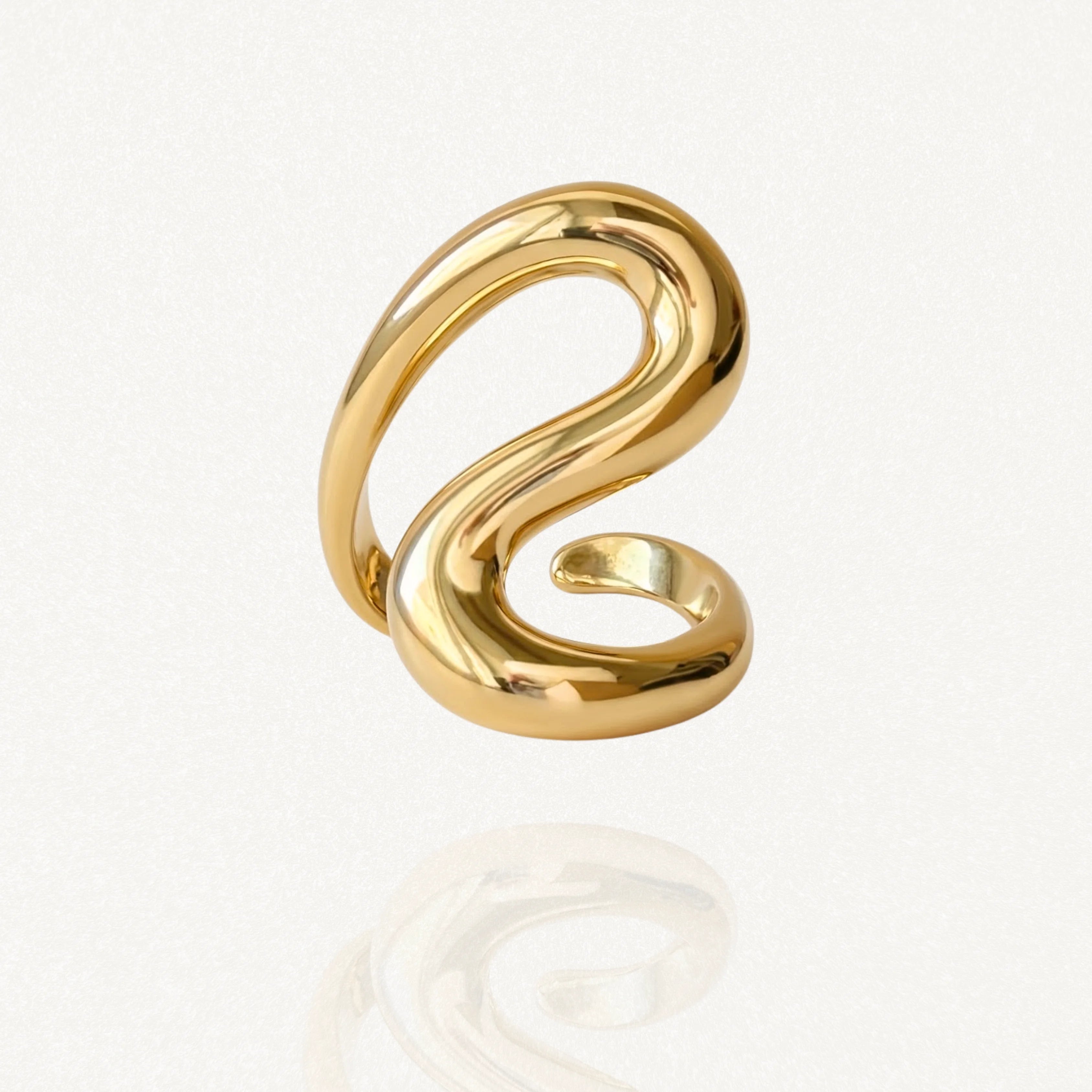 Bague large dorée au design sculptural en forme de S ou de vague fluide, vue sur fond blanc.