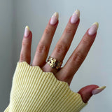 Bague large en acier inoxydable doré, motif fleurs ajouré, portée sur main aux ongles décorés.