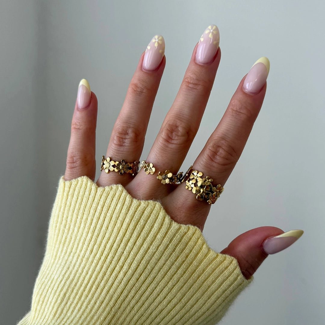 Bague en acier inoxydable dorée, motif floral ajouré de petites fleurs, portée sur un doigt.