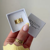 Bague fleur dorée en acier inoxydable dans sa boîte cadeau et portée par une main au pouce.