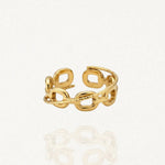 Une bague ouverte dorée en acier inoxydable avec un motif de maillons de chaîne entrelacés et une bande texturée, posée sur une surface blanche réfléchissante.